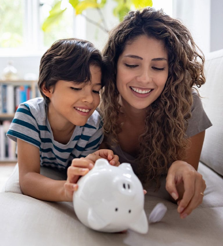 A woman and child putting coins in a piggy bank at home.