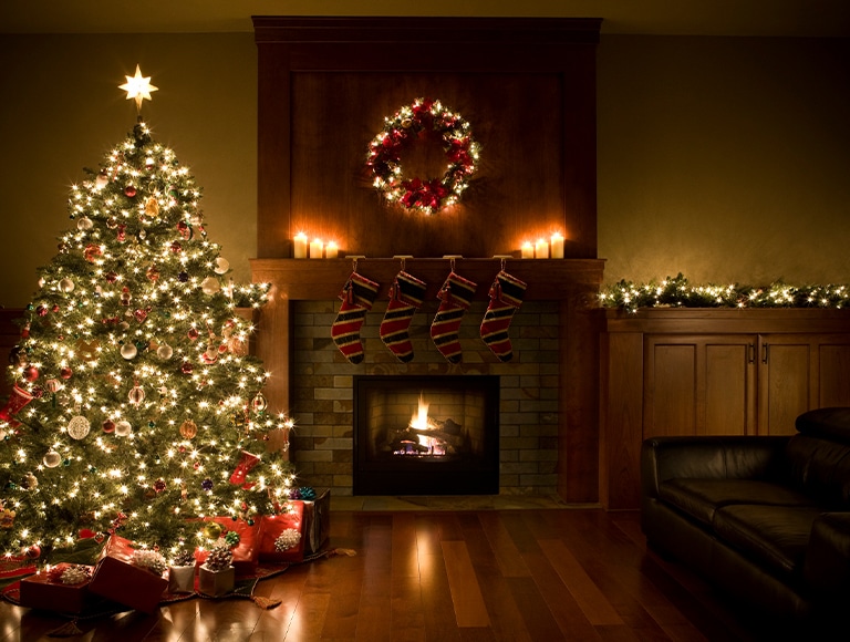 Cozy living room with a decorated Christmas tree, stockings, and a glowing fireplace.