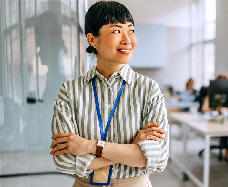 A woman in a striped shirt stands confidently in a modern office setting.